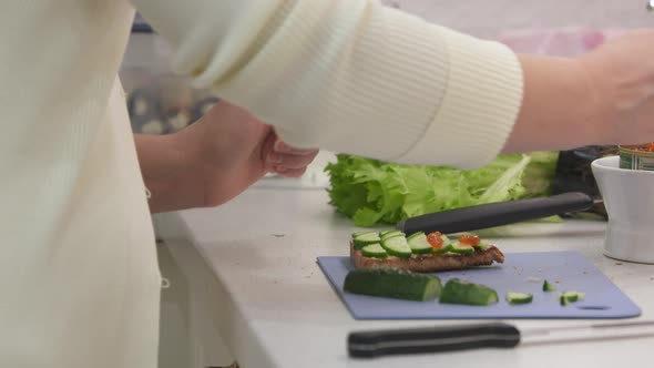Woman Cooking Festive Dinner in the Kitchen Making Toast with Cucumber and Caviar alt