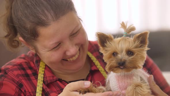 Smiling Woman Holding Cute Puppy Dressed in Pink Sweater alt