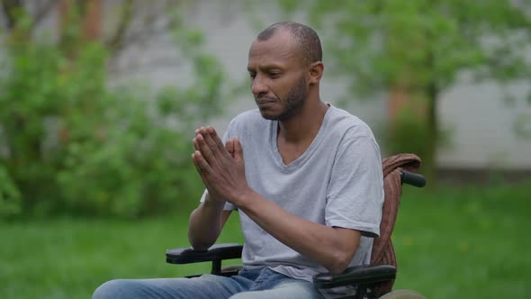 Sad Concentrated African American Man in Wheelchair Praying in Summer Garden Outdoors alt