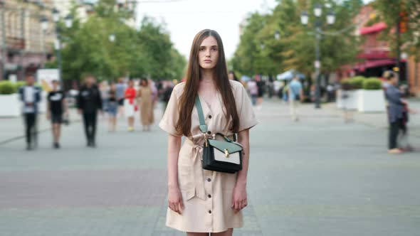 Time Lapse Portrait of Pensive Young Girl Standing Outside in Urban Street While People are Walking alt