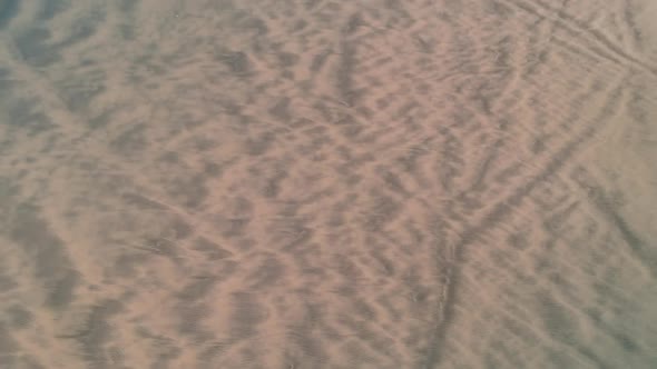 Revealing drone shot of incoming waves on a long beach with dunes on the rigth side alt