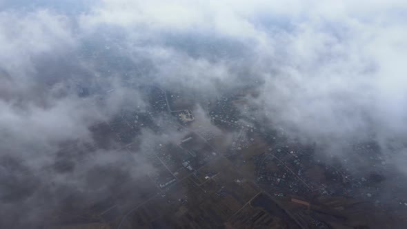 Aerial View From High Altitude of Distant City Covered with Puffy Cumulus Clouds Flying By Before alt