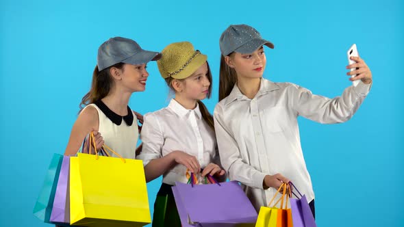 Three Teenagers Make Selfies with Colorful Packages. Blue Background alt