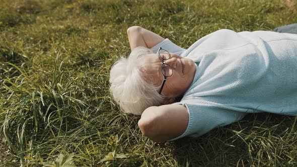 Mature Woman Lying on the Grass with Hands Under Her Head. Close Up Shot alt