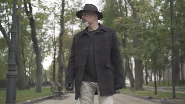 Portrait of Elegant Careful Detective Walking Along Park Alley, Stopping, and Looking Away alt