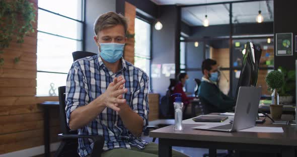 Caucasian man wearing face mask using hand sanitizing at modern office alt