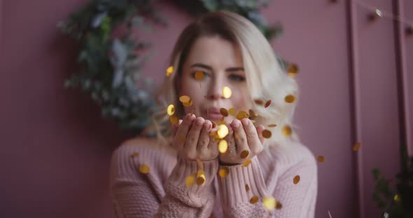 Beautiful Woman in Sweater Blows Shiny Confetti From Her Hands To the Camera in Slow Motion alt