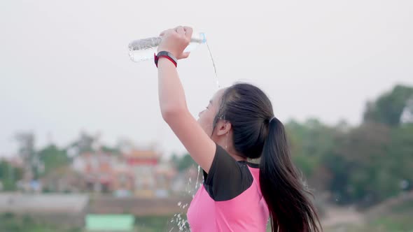 Sport Asian woman pouring water on head to refresh after run outdoor exercise in pink sportswear alt