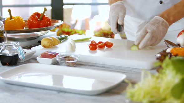 Hand with Knife Cuts Cucumber. alt
