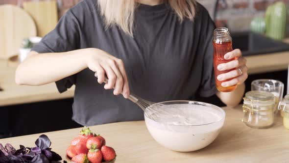 Young Woman Pours Honey From Transparent Glass Jar at Table