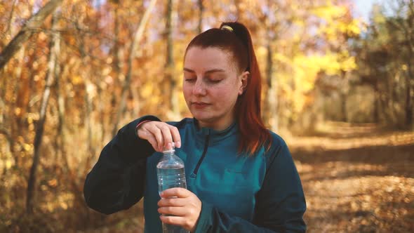 Active Young Girl Runner in Sportswear Drinks Water After Jogging Workout in the Autumn Park Taking
