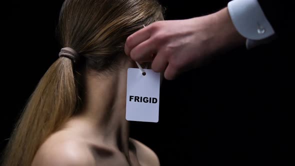 Man Hand Putting Frigid Label on Female Ear Imposing Sex Insecurities on Partner alt