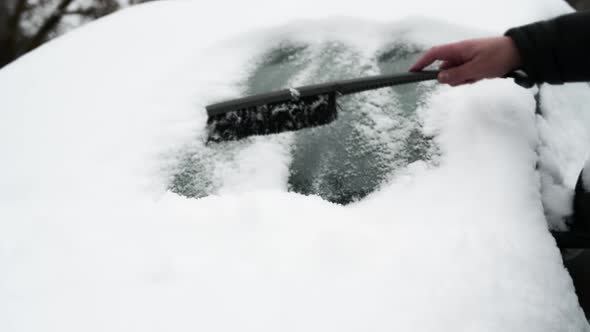 a man in the winter cleans the car from snow. Removing snow from a car windshield.