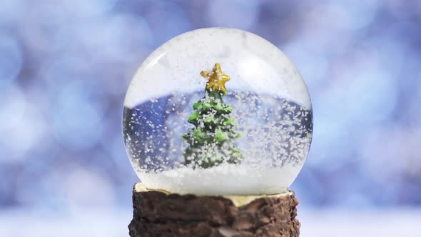 Close-up of Snowflakes Swirling Around a Christmas Tree Inside a Glass Ball alt