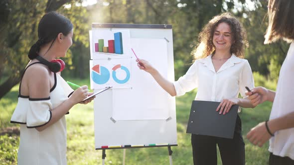 Group of Young Cheerful Startupers Standing in Spring Summer Park in Sunshine Talking Analyzing alt