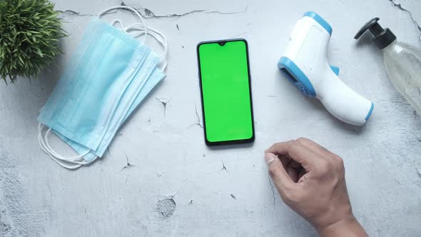 Flat Composition of Smart Phone Mask Thermometer and Sanitizer on Table alt