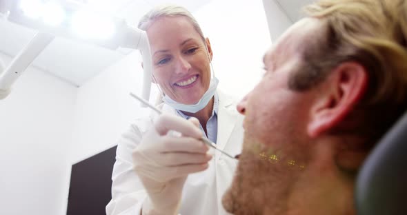 Female dentist examining male patient with dental tools alt