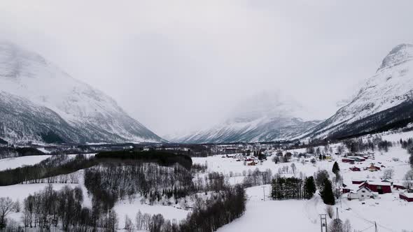 Misty mountains and snowed in village in white Manndalen valley, winter aerial alt