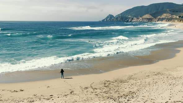 A Girl Standing on the Shore of a Sandy Beach of the Pacific Ocean alt