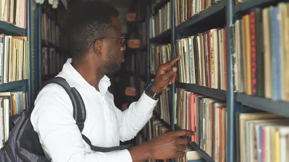Young Male Student Choosing Book Between Shelves in the Library. alt