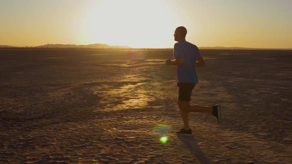 Athletic man working out with battle ropes on a dry lake at sunset alt