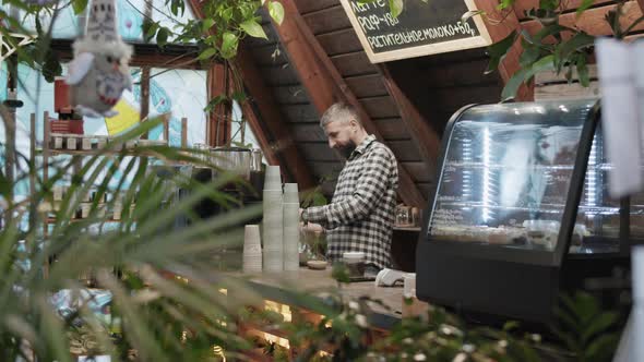 Male barista in checkered shirt prepares beverage