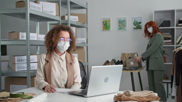 Online Shop Young Woman in Medical Masks Seller and Her Female Colleague Sell Goods Via Internet and alt