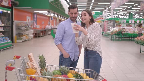 Attractive happy millennial couple checking a grocery bill receipt in supermarket alt