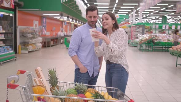 Attractive happy millennial couple checking a grocery bill receipt in supermarket