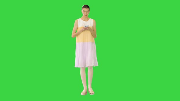 Young Beautiful Girl in Whiteyellow Dress Walks Typing on Mobile Phone on a Green Screen Chroma Key