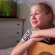 White Teenage Girl Sings Song Leaning on Acoustic Guitar While Sitting in Room - VideoHive Item for Sale