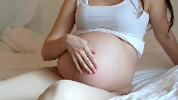 A pregnant woman stroking her bare pregnant belly. alt