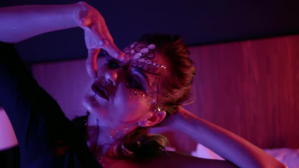 Graceful Woman with Shiny Stage Makeup Is Posing for Camera in Dark Bedroom Portrait Shot alt