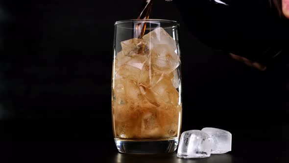 Pouring Cola with ice cubes in glass on black background. Close up.