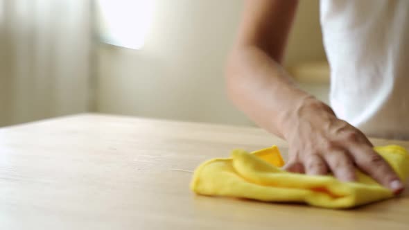 Housewife Wiping Spilled Coffee or Tea From a Wooden Kitchen Table. Female Using a Household Cleaner alt