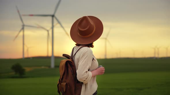 Beautiful girl in a hat with a camera in a field with windmills alt