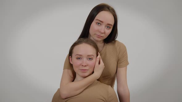 Front View Young Woman Touching Face of Twin Sister Posing at Grey Background alt