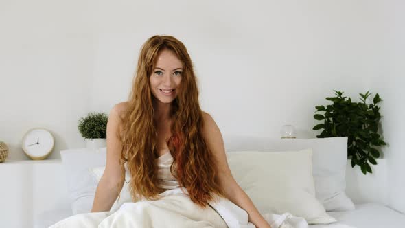 Portrait of a happy smiling woman in pajamas on a bed  in white bedroom