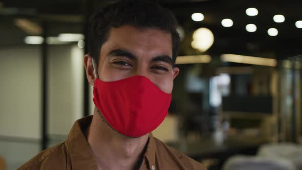 Portrait of a mixed race businessman wearing face mask looking at camera in modern office alt