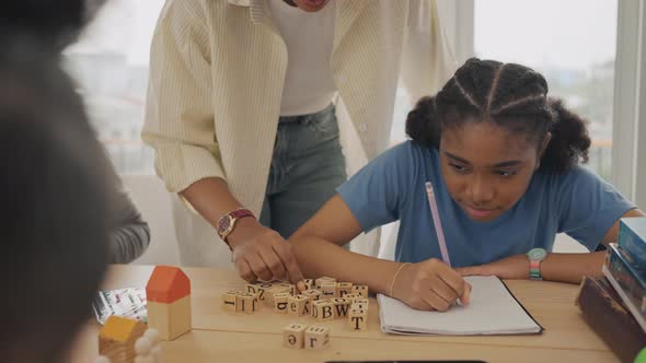 African American female teacher standing with pupils teaching writing lesson in modern classroom. alt