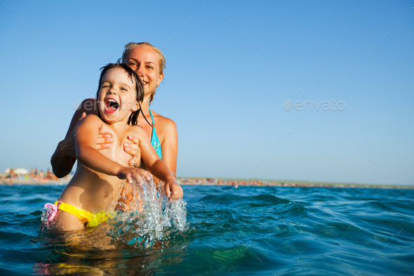 Young mother standing in water and playing with her small daughter
