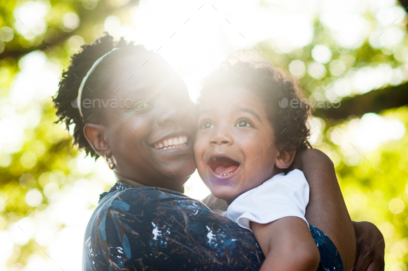 African mom smiling to the camera holding her toddler boy in her arms - Stock Photo - Images
