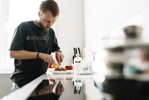 Photo of caucasian young man eating croissant while having breakfast
