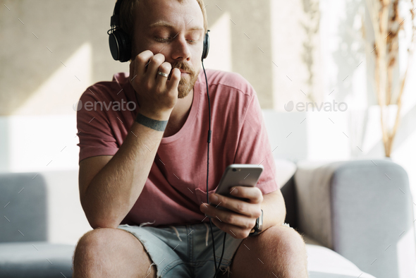 Photo of man using mobile phone and headphones while sitting on sofa