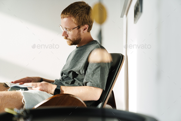 Photo of thinking young man reading book while sitting in armchair