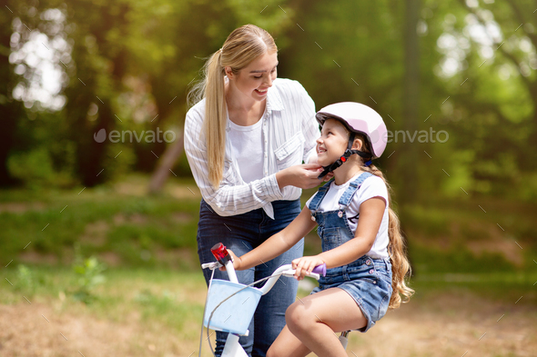 Mother Teaching Daughter To Cycle, Putting Helmet On Kid Outdoor