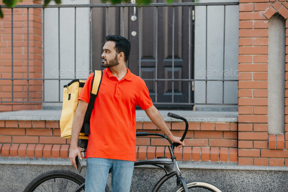Work in city. Serious deliveryman with beard with backpack and bicycle, holding smartphone and - Stock Photo - Images