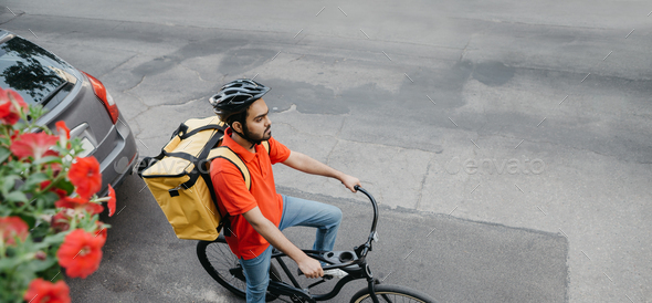 Online delivery service. Courier in helmet with big yellow backpack on bicycle