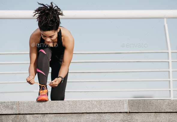 Start of morning workout. African american young woman in sportswear with fitness tracker tying