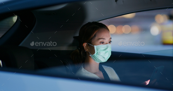 Woman wear medical mask and use of mobile phone sit inside the car